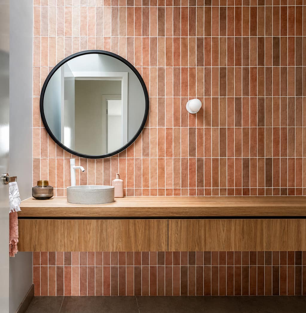 Oak vanity with a round mirror and warm pink finger-tile splashback