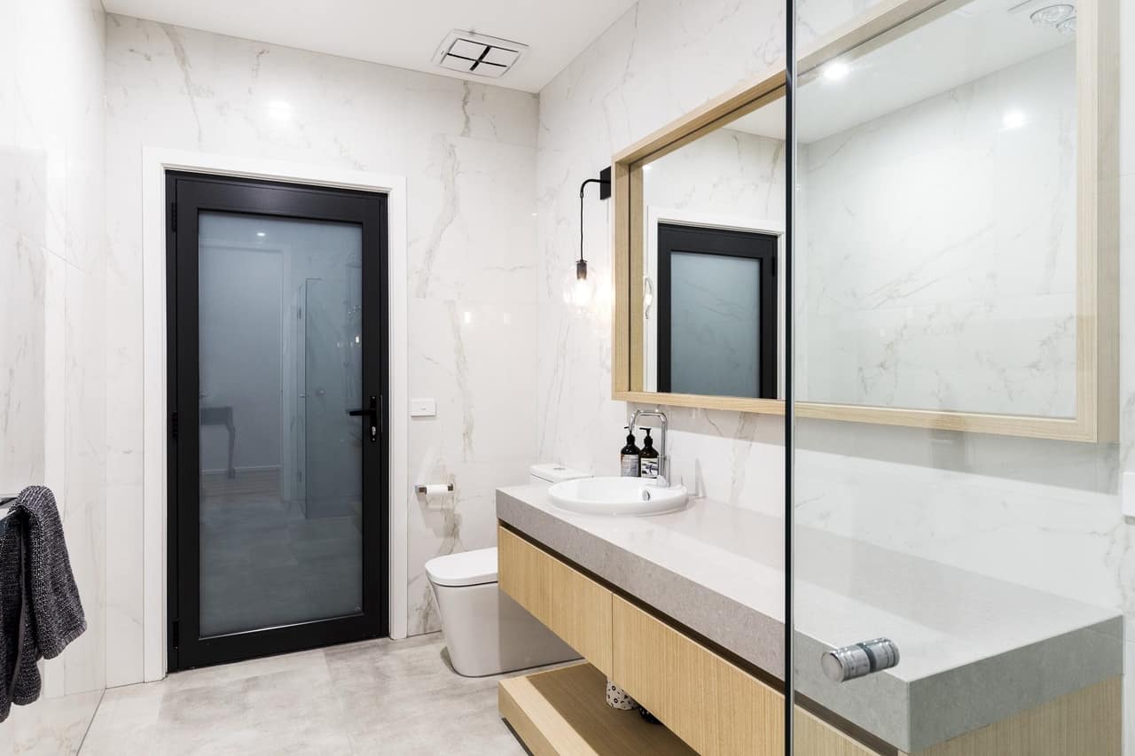 Light oak floating vanity with thick grey stone benchtop and inset basin in a marble-tiled bathroom