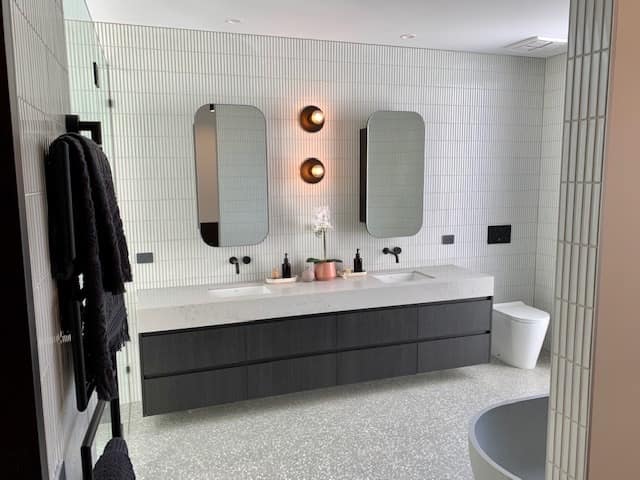Charcoal floating double vanity with white stone top and pill-shaped mirrors on white kit-kat tiles