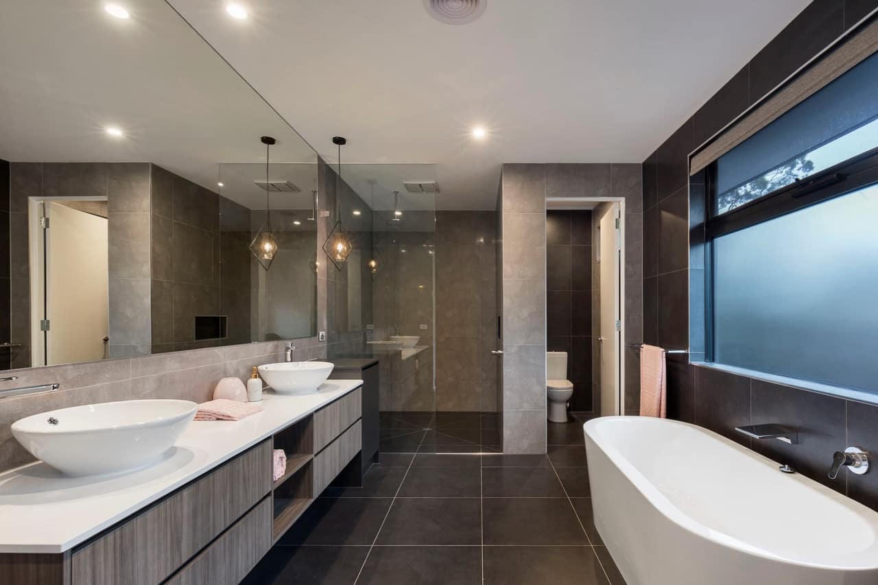 Dark-tiled ensuite with grey woodgrain floating vanity, twin white counter-top basins and freestanding bath