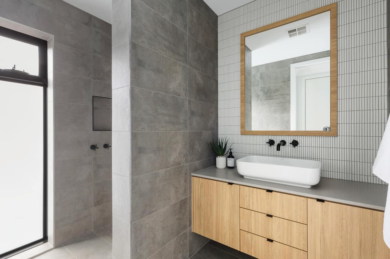 Oak floating vanity with grey stone top and white vessel basin against white kit-kat tiles and matte black tapware