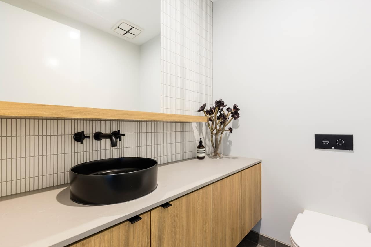 Powder room with oak floating vanity, grey stone top, round matte black basin and black wall-mounted tapware