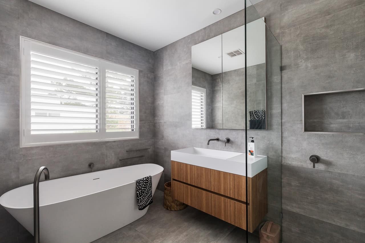 Timber floating vanity with white benchtop and mirrored cabinet against grey concrete-look tiles